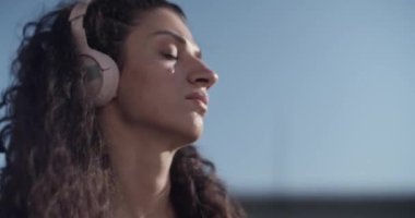 El kamerasıyla çekilmiş, dalgalı siyah saçlı, kablosuz kulaklıkla müzik dinleyen ve sabah sokakta dans ederken kafasını oynatan genç bir kadın fotoğrafı.