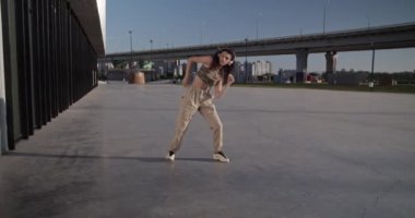 Şık, genç bir dansçının kollarını oynatarak ve bükerek müzik dinleyerek ve modern binanın önünde sabahları performans sergilemesini izlemek.