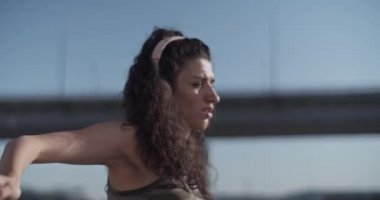 Şehirde güneşli bir sabahta dans ederken kablosuz kulaklıkla müzik dinleyen ve omuzlarını hareket ettiren genç bir bayan dansçının el kamerasıyla çekilmiş fotoğrafı.