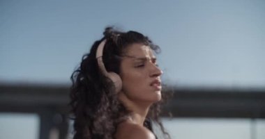 Düşük açılı bir el kamerası ile çekilmiş genç bir kadın kablosuz kulaklıkla müzik dinliyor ve mavi gökyüzüne karşı dans ederken dalgalı siyah saçlarını sallıyor.