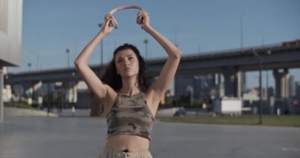 Powiększ Ujęcie Młodej Kobiety Kamuflażu Zakładającej Słuchawki Bezprzewodowe Patrzącej Kamerę — Wideo stockowe