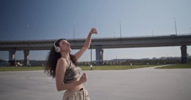 Moda kıyafetleri ve kablosuz kulaklıklar takmış müzik dinleyip, hafta sonu bulutsuz mavi gökyüzü ve briç eşliğinde hip hop dansı yapan genç esmerin el kamerasıyla çekilmiş bir fotoğrafı.