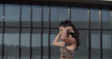 Genç bir kadının kablosuz kulaklık taktığı ve şehir sokaklarında camdan duvarları olan modern binaya karşı kapalı gözlerle müzik dinlediği görüntüyü yakınlaştır.