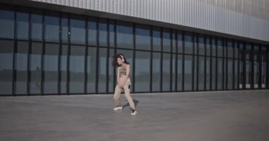 Sabahları şehrin sokaklarında camdan duvarları olan modern binaya karşı dans eden sıradan giyinmiş genç bir kadının el kamerasıyla çekilmiş fotoğrafı.