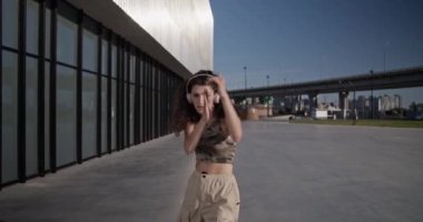 Genç bir kadının kablosuz kulaklıklarla müzik dinlerken ve modern şehrin sokaklarında dans ederken görüntülerini izliyoruz.