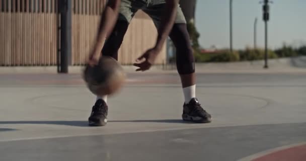 市内の裁判所で晴れた夏の日にストリートボールの訓練中に地面にボールをドリブル匿名の黒人スポーツマンのハンドヘルドショット — ストック動画