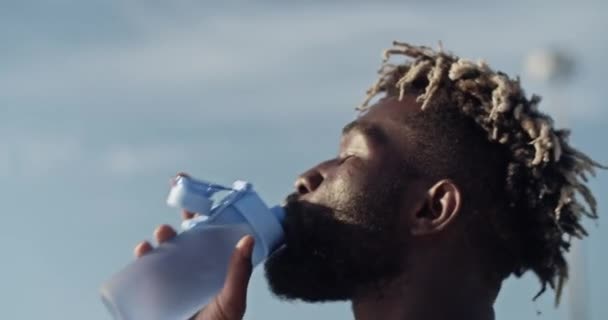 在阳光明媚的夏日 一名非洲裔美国男子运动员从下面抓拍的裸体照片中 在蓝天和瓶子的衬托下喝水 — 图库视频影像