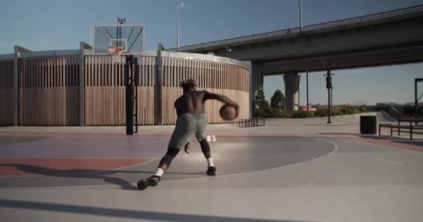 在城市桥头堡附近的球场训练中 一名赤身裸体的黑人运动员手持式投篮和运球入篮筐 — 图库视频影像