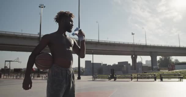 在阳光明媚的夏日 穿着便衣的非洲裔美国男子运动员在训练期间 从下面抓拍到的照片 他们一边喝着瓶子里的水 一边看着桥和蓝天 — 图库视频影像