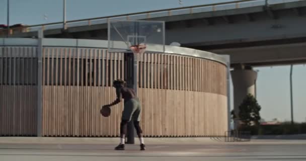 市内のスポーツグラウンドでストリートボールトレーニング中にフープの近くに立っている間 裸の胴ドリブルボールを持つ匿名の黒のスポーツマンのビューでズーム — ストック動画