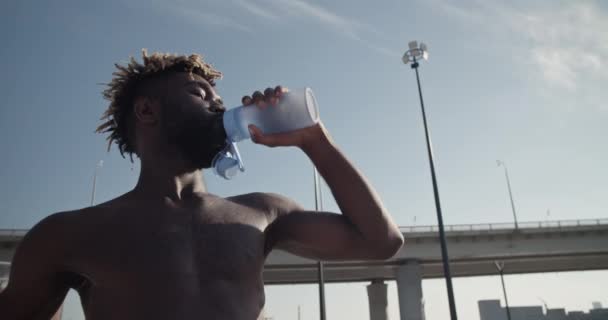 在阳光明媚的夏日 穿着便衣的非洲裔美国男子运动员在训练期间 从下面抓拍到的照片 他们一边喝着瓶子里的水 一边看着桥和蓝天 — 图库视频影像
