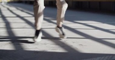 Tozlu beton zeminde dans eden şık pantolonlu ve spor ayakkabılı kapalı otoparktaki performans sırasında elde çekilmiş bir kadın fotoğrafı.