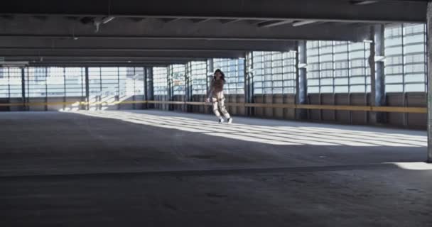 広々とした空の駐車場の建物の中で踊りながら 日光の下を歩くとジェスチャーでカジュアルな服で若い女性の手持ち撮影 — ストック動画