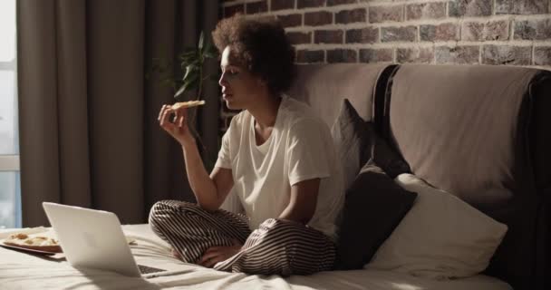 Black Female Pajama Curly Hair Biting Pizza Watching Film Netbook — Stock Video