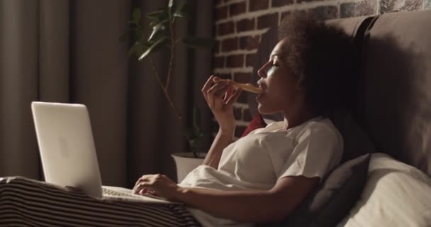 Handheld Shot Black Woman Gryzienie Żucie Pizzy Podczas Odpoczynku Łóżku — Wideo stockowe