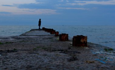 Bulutlu bir günde bir adam kıyıda duruyor. Güzel manzara.