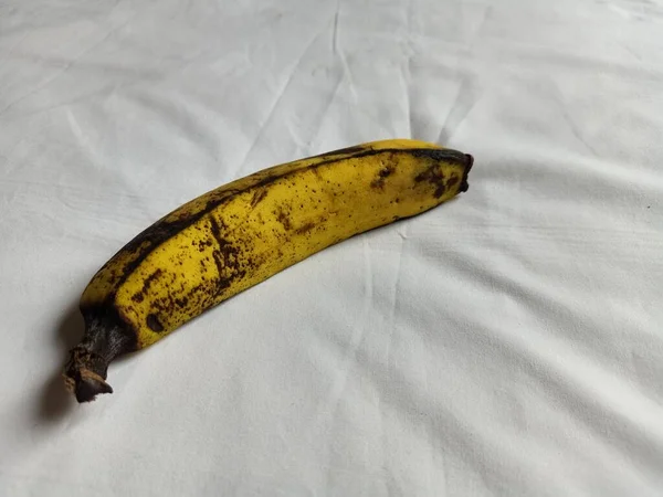 Almost rotten or overripe banana. Yellow banana isolated on a white fabric background. The concept of conservation and quality of food.