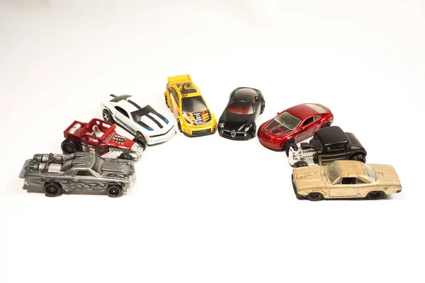 Bir grup Hot Wheels oyuncağı beyaz arka planda yarım daire şeklinde dizilmiş.