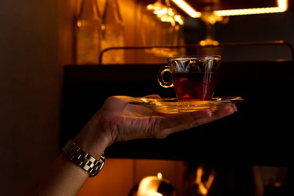 Cam ambarın önünde bir bardak çayı tutan el.