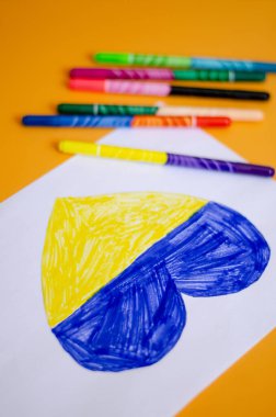 high angle view of modern felt pens near paper with drawn heart and ukrainian flag on yellow  clipart
