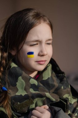 Yanağında Ukrayna bayrağı ve kamuflaj ceketi olan çocuk.