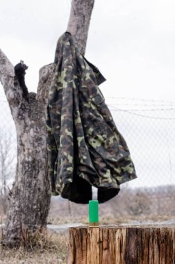shotgun shell on wooden stump near camouflage jacket in woods clipart