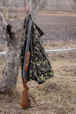 Ormanda tüfeğin yanındaki ağaçta asılı kamuflaj ceketi.
