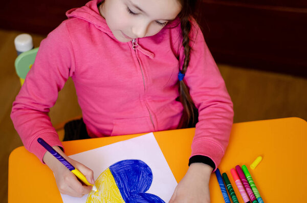 высокий угол обзора девушки, рисующей сердце с украинским флагом на желтом столе 