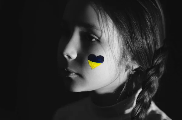 Ukrayna bayrağını siyah yanağına boyamış hayal kırıklığına uğramış bir kızın monokrom fotoğrafı. 