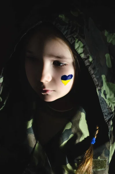 Enfant bouleversé avec drapeau ukrainien peint sur la joue isolé sur noir — Photo de stock