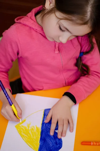 High angle view of kid drawing heart with ukrainian flag colors on yellow desk — Stock Photo