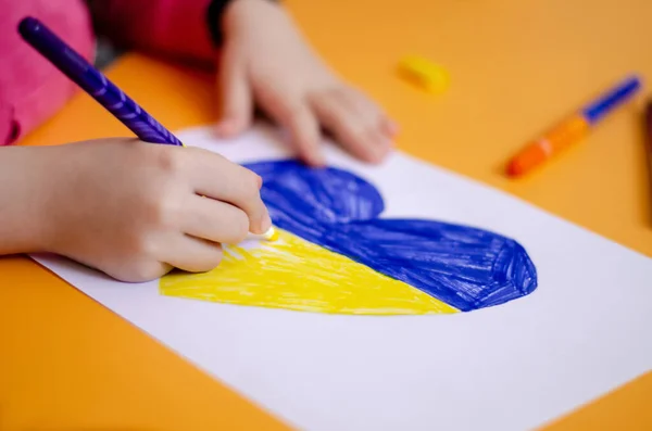 Ausgeschnittene Ansicht eines Kindes, das Herz mit ukrainischer Flagge auf gelbem Schreibtisch zeichnet — Stockfoto