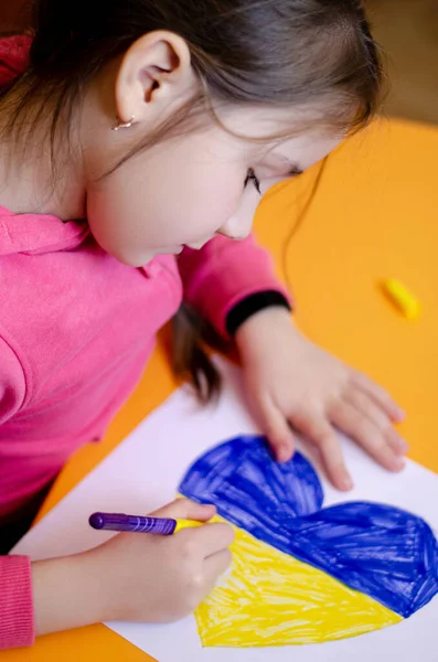 Vista ad alto angolo del cuore disegno bambino con colori bandiera ucraina sulla scrivania gialla — Foto stock