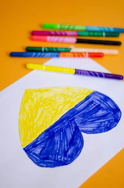 Vista de ángulo alto de los bolígrafos de fieltro modernos cerca de papel con corazón dibujado y bandera ucraniana en amarillo - foto de stock