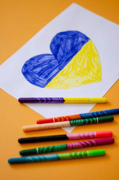 High angle view of felt pens near paper with drawn heart and ukrainian flag on yellow — Stock Photo