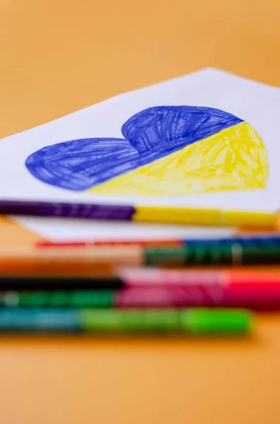 Blurred felt pens near paper with drawn heart and ukrainian flag isolated on yellow — Stock Photo