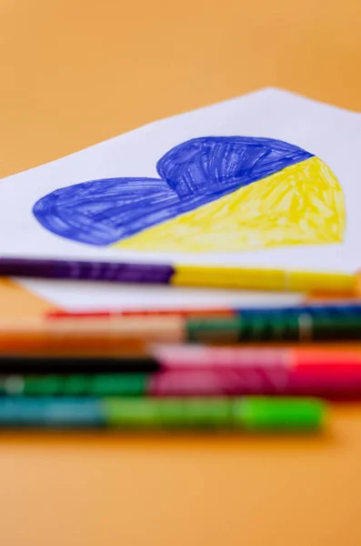 Plumas de fieltro borrosas cerca de papel con corazón dibujado y bandera ucraniana aislada en amarillo - foto de stock