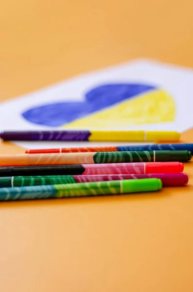 Modern felt pens near blurred paper with drawn heart and ukrainian flag on yellow — Stock Photo