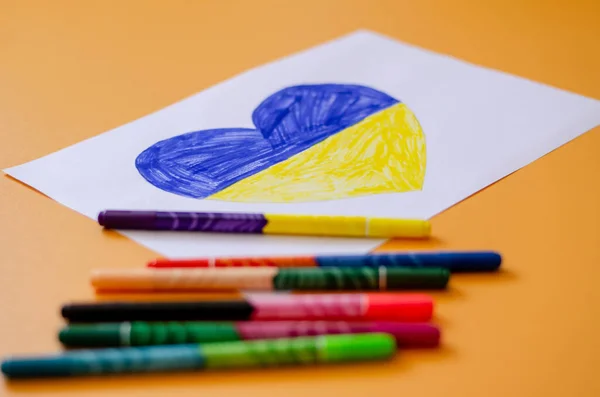 Blurred felt pens near paper with drawn ukrainian flag in heart on yellow — Stock Photo