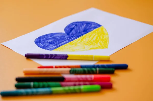 Canetas de feltro borradas perto de papel com bandeira ucraniana desenhada no coração em amarelo — Fotografia de Stock