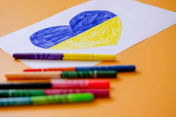 Felt pens and paper with drawn ukrainian flag in heart on yellow — Stock Photo