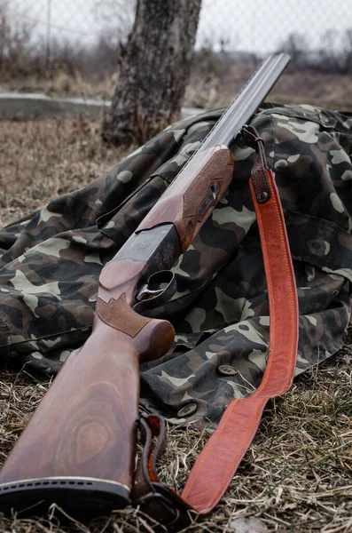 Close up view of military rifle on camouflage jacket in forest — Stock Photo