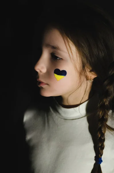 Frustrated kid with painted ukrainian flag on cheek isolated on black — Stock Photo