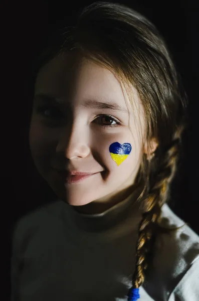 Cheerful girl with painted ukrainian flag on cheek isolated on black — Stock Photo