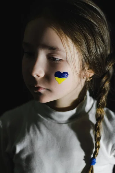 Frustrated girl with painted ukrainian flag on cheek isolated on black — Stock Photo