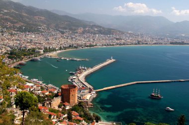 Panoramic view of Alanya city with red tower and ships in the foreground with mountains in the background in the south of Turkey