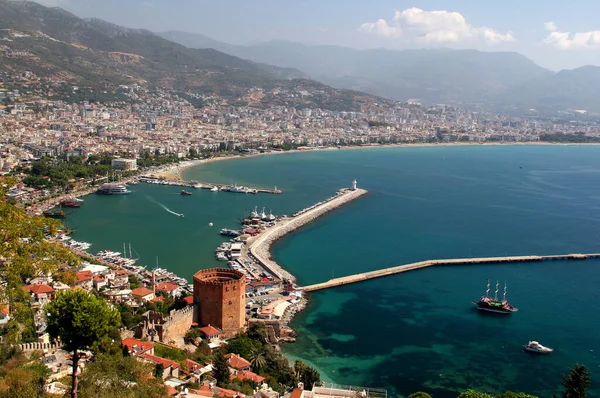 Alanya 'nın panoramik manzarası, kırmızı kulesi ve ön planda gemileri ile Türkiye' nin güneyinde dağlar var.
