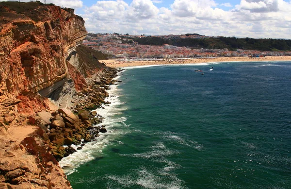 Overhanging cliffs and coastline of Nazare beach and azure waters of the Atlantic Ocean, Portugal