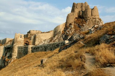 Türkiye 'nin Doğu Anadolu bölgesinde, bulutlu mavi gökyüzüne karşı yüksek bir kayanın üzerinde yer alan ve giriş kapısı bulunan Van Kalesi' nin eski kısmının görüntüsü