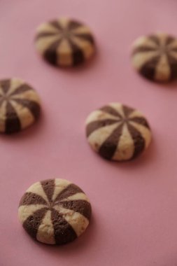 Pembe arka planda yuvarlak çikolatalı sarmal kurabiyeler.